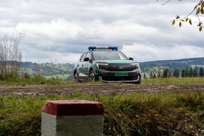 Na tle pagórków stoi samochód zakupiony w ramach projektu. Przed nim słupek graniczny.