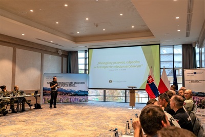 Uczestnicy projektu słuchają wystąpienia prelegenta. Na monitorze wyświetla się prezentacja. Po bokach ekranu stoi ścinka i rolup projektowy.