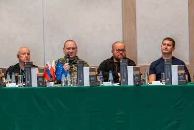 Uczestnicy szkolenia siedzą przy stole prezydialnym, jeden z nich przemawia do mikrofonu. Na stole flagi słowacji, polski i unijna.