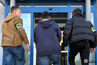 Dwóch funkcjonariuszy straży granicznej w strojach cywilnych prowadzi zatrzymanego cudzoziemca do siedziby placówki sg w krakowie