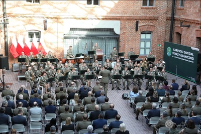 ujęcie od tyłu publiczności obecnej na koncercie - kilkaset osób. na scenie gra orkiestra reprezentacyjna sg a przed nią dyryguje dyrygent