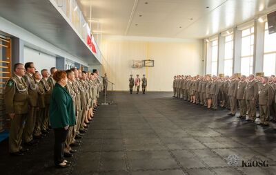 hala sportowa - ujęcie na całe pomieszczenie. po lewej kadra kierownicza oddziału, po prawej mianowani i odznaczeni funkcjonariusze i pracownicy oddziału - kilkaset osób. daleko na srodku poczet sztandarowy kaosg