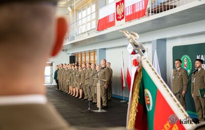 hala sportowa - ujęcie przez sztandar kaosg. widać kadrę kierowniczą oddziału i organizatorów uroczystości - stoją na baczność podczas śpiewania hymnu RP