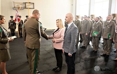 Hala sportowa. generał gratuluje pracownikowi - kobiecie po wręczeniu odznaki kaosg na drewnianej tabliczce