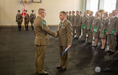 hala sportowa. kapelan kaosg wręcza medal jednemu z funkcjonariuszy, w tle uczestnicy uroczystości