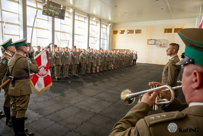 hala sportowa - ujęcie przez grającego na trąbce funkcjonariusza na całe pomieszczenie. po lewej poczet sztandarowy. w tle odznaczeni i mianowani funkcjonariusze i pracownicy stojący na baczność w kilku kolumnach