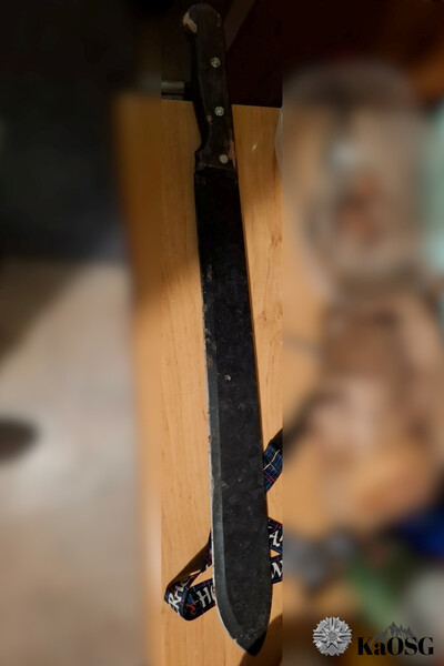 Na stole leży czarna maczeta, reszta obrazu jest zamazana.