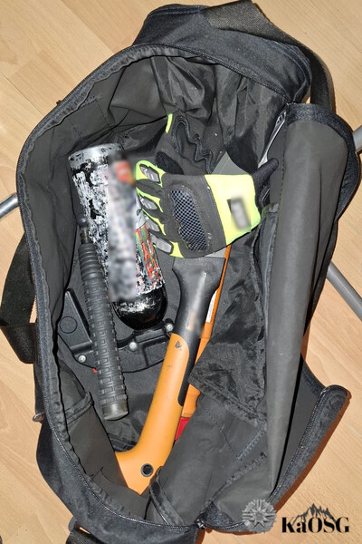 Na podłodze leży torba sportowa, w której znajduje się pojemnik na gaz pieprzowy, siekiera, rękawice gumowe, i pałka