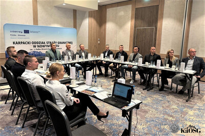 uczestnicy spotkania - kilkanaście osób - siedzą przy stole ułożonym w kształcie litery u. słuchają prelegenta.