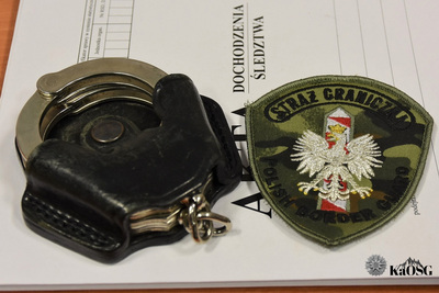 na aktach dochodzenia leżą kajdanki i emblemat straży granicznej