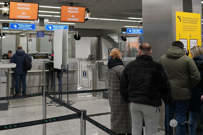 Na zdjęciu widać halę do odpraw na lotnisku. Po prawej stronie widać osoby czekające na odprawę. Na wprost widać budkę kontrolerską, funkcjonariusz dokonuje odprawy granicznej.