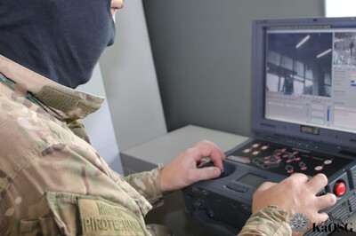 zamaskowany pirotechnik sprawdza bagaż przy użyciu robota pirotechnicznego. na monitorze urządzenia widać oglądany przez niego przedmiot