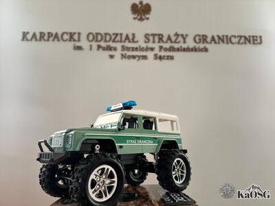 Na zdjęciu samochód zabawka marki Land Rover, jakim na co dzień posługują się funkcjonariusze Karpackiego Oddziału SG w trakcie patroli. W tle napis Karpacki Oddział Straży granicznej im. 1 Pułku Strzelców Podhalańskich