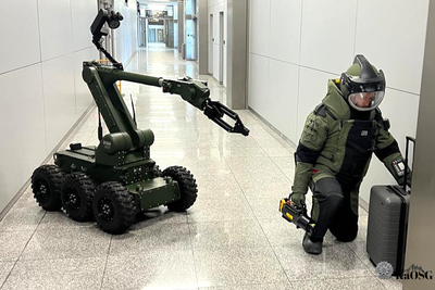 Na zdjęciu widać mężczyznę ubranego w kombinezon antywybuchowy dla saperów, który sprawdza walizkę czarną czy nie ma w niej bomby