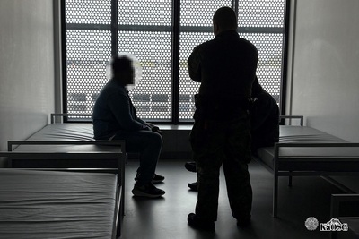 obywatel indii siedzi na łóżku w pomieszczeniu w którym przebywa do czasu odlotu do Zjednoczonych emiratów arabskich. Towarzyszy mu funkcjonariusz sg