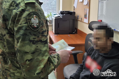 Zatrzymany lankijczyk siedzi przy biurku. Widać też ramię funkcjonariusza sg