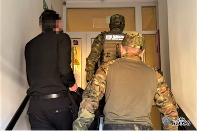 Dwaj funkcjonariusze  prowadzą po schodach zatrzymanego cudzoziemca