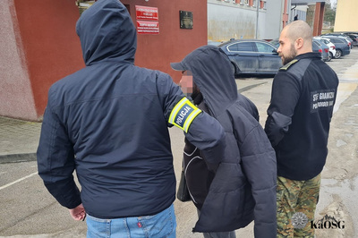 Cudzoziemiec stoi pomiędzy funkcjonariuszem Policji i Straży Granicznej przed budynkiem Placówki SG w Kielcach