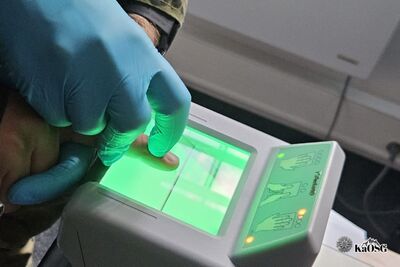 Na zdjęciu widoczne urządzenie do czytania odcisków palców. Widoczna dłoń w rękawiczce trzymająca palec drugiej osoby.