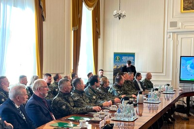 Widok z boku na rząd uczestników w mundurach siedzących przy stole w bogato zdobionej sali z wysokimi oknami. W tle ekran z mapą Polski i logotypy Straży Granicznej.