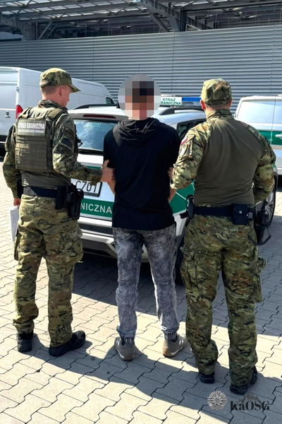 Na zdjęciu widać trzech mężczyzn stojących przed budynkiem przed samochodem służbowym oznakowanym jako Straż Graniczna