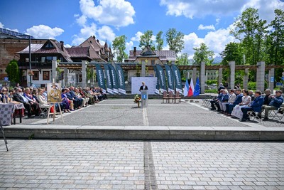 ujęcie ogólne na plac grunwaldzki. jeden z mężczyzn przemawia do mikrofonu. po lewej i prawej stronie siedzi kilkudziesięciu uczestników uroczystości, w tle za przemawiającym powiewają żagle z napisem zakopane