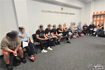 13 zatrzymanych cudzoziemców siedzi na krzesłach w pomieszczeniu placówki sg. część z nich trzyma w rękach dokumenty.