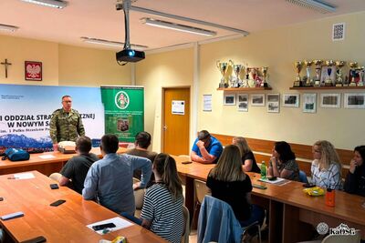 Grupa osób, najprawdopodobniej uczestnicy szkolenia siedzą w pomieszczeniu biurowym. W tle pomieszczenia biurowe oraz ekran multimedialny.