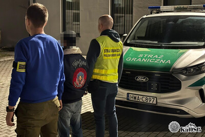 Na zdjęciu widać trzy osoby po lewej stronie. Jest ciemno, późny wieczór. Po prawej stronie widać częściowo samochód oznakowany srebrny z zielonymi napisami i passami.