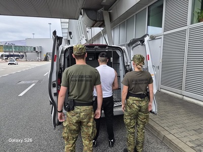 dwoje funkcjonariuszy SG prowadzi zatrzymanego mężczyznę do samochodu służbowego